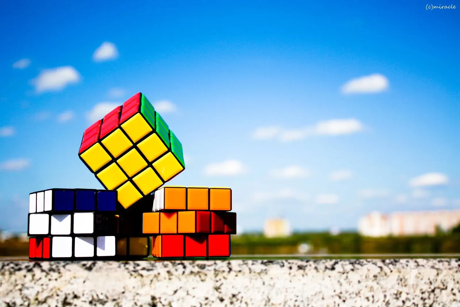Stack of colourful puzzle cubes on a wall against a bright blue sky